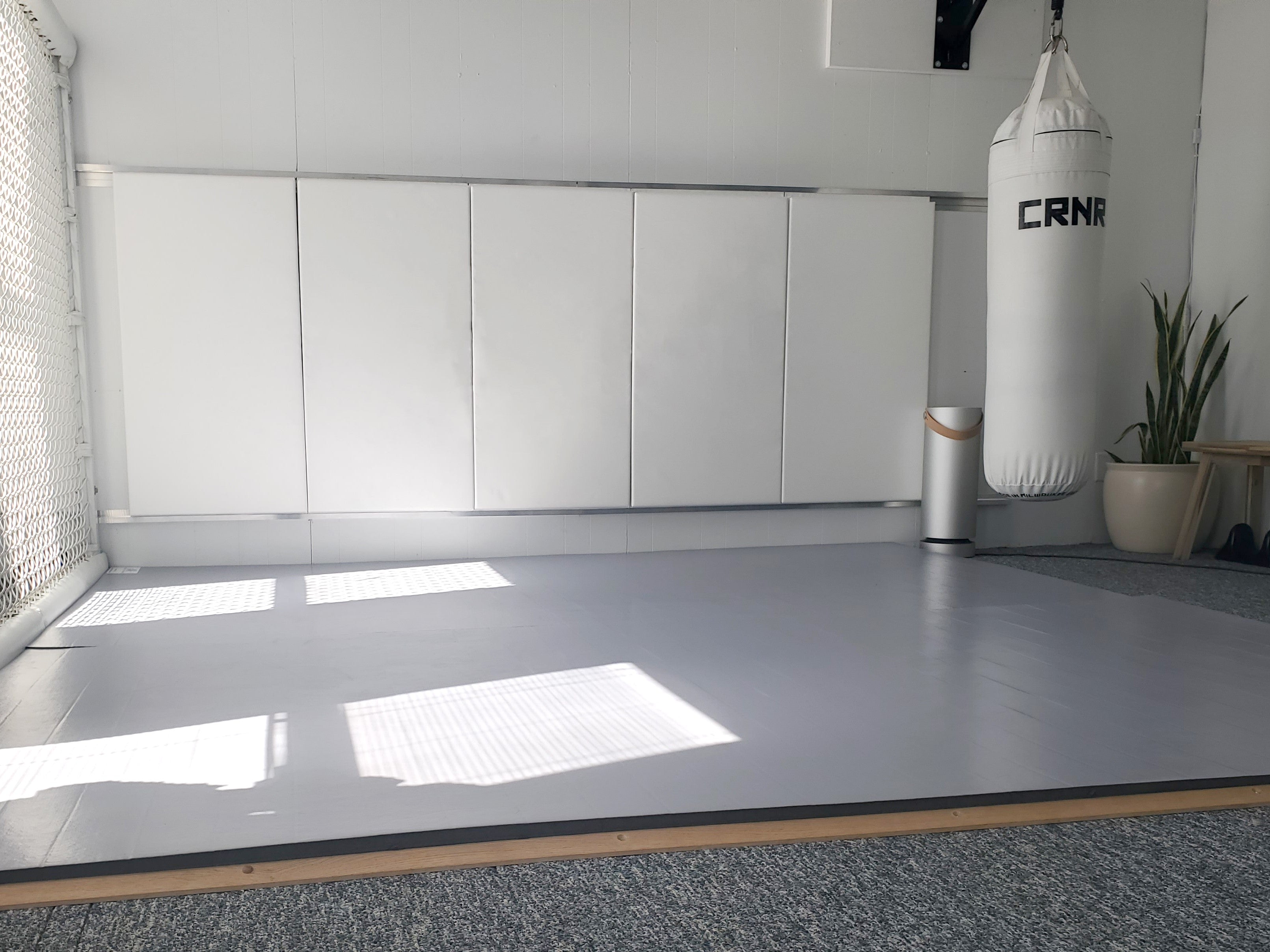 Home martial arts room with grey wrestling mats and white wall pads