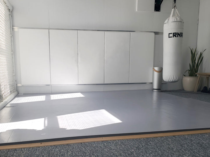Home martial arts room with grey wrestling mats and white wall pads